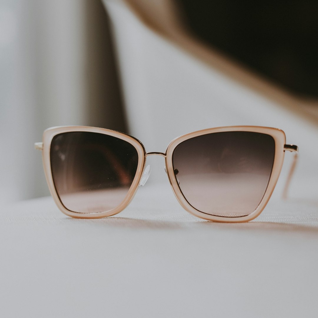 Light pink cat-eye sunglasses with gold temples on a textured surface.